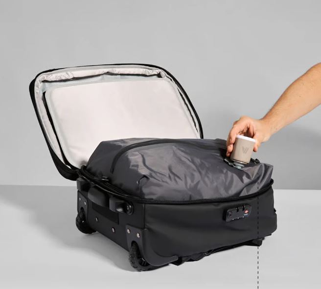 Opened Black wheeled suitcase bag showing a grey compression bag inside, with a hand holding a white device to the compression section
