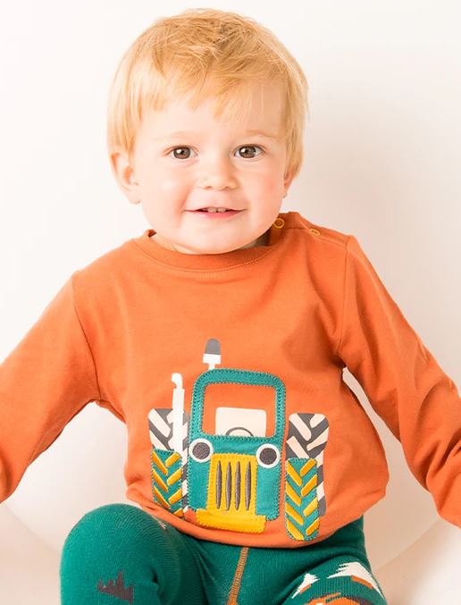 small child wearing a orange top with a tractor on it and bright green trousers