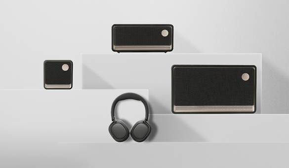 image with three dark grey square/rectangle speakers of varying sizes on a white background with a pair of headphones in the middle