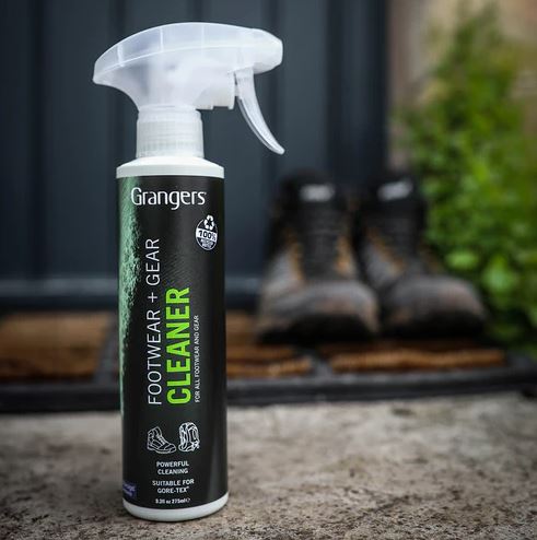 Image of Grangers Footwear + Gear Cleaner spray bottle on a concrete surface, with a pair of hiking boots blurred in the background. 