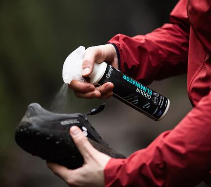 Image showing a person spraying a waterproofing product labeled 'Odour Eliminator' into a black walking shoe. 