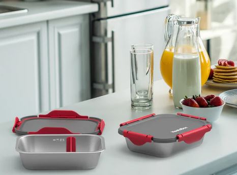 two silver meal meal prep dishes with black and red lids on a kitchen counter 