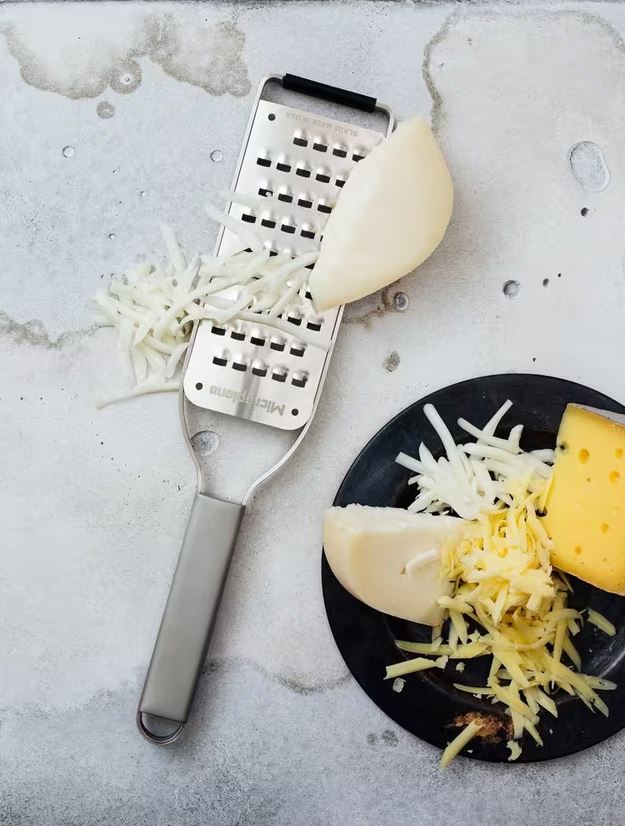 ribbon grater with block of cheese and grated cheese on a plate to the right 