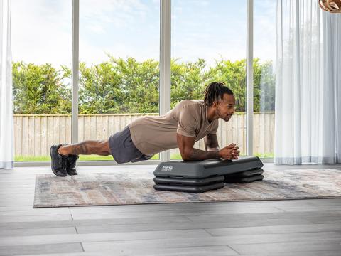 man planking with his arms on a grey aerobic step 