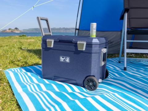 blue cool box with wheels and a handle on a blue striped picnic blanket over grass