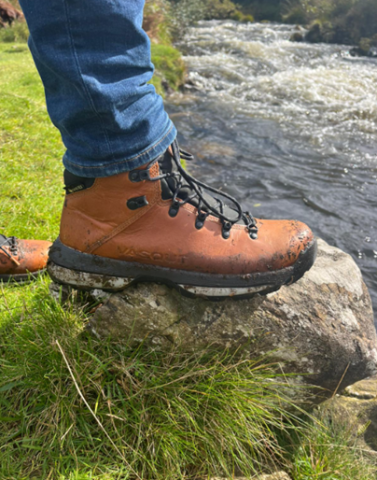 persons foot wearing a brown hiking boot standing on a rock 