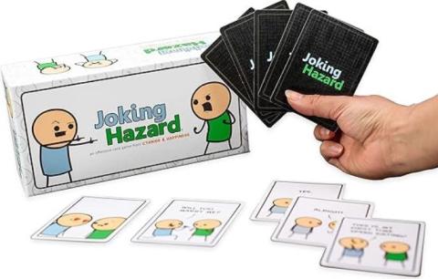 hand holding black Joking Hazard cards above the white game box with cards on a white table 