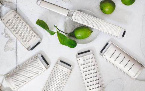 5 different graters and a zester ona white table with green fruit in the middle 