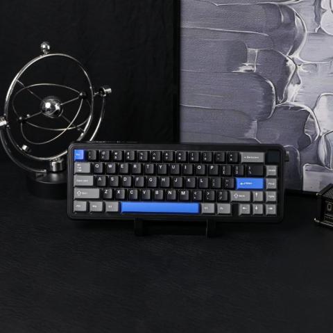 black small 66 key keyboard with grey keys and blue accent space and enter keys on a black desk background