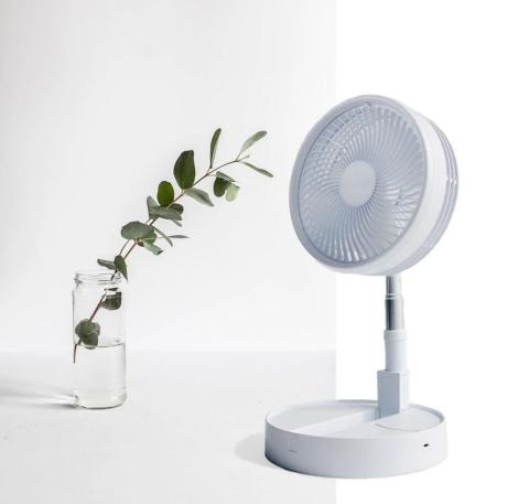 white fan standing on a white table, with a plant in a glass vase next to it 