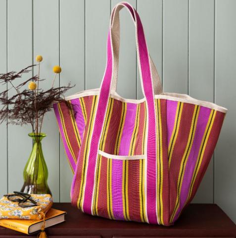pink, red, yellow and white striped beach tote back on a wooden table next to a vase of flowers and some books