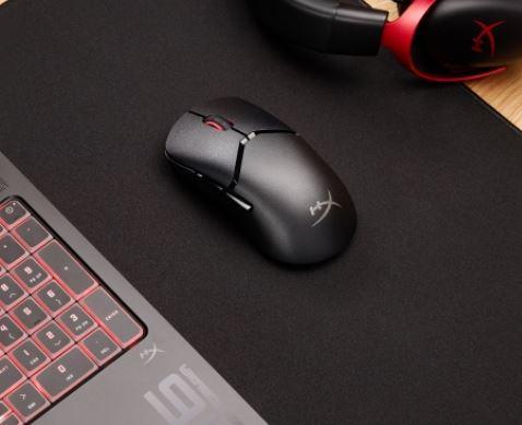 black gaming mouse on a black mouse mat, with a laptop next to it 