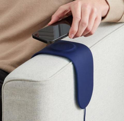 blue silicone pad over arm of white sofa chair, with persons hand placing mobile phone on it