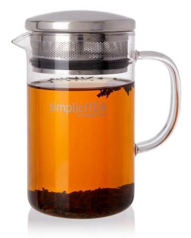 Clear glass tea infuser jug with amber-coloured tea brewing in it with loose leaf tea settled at the bottom, and some floating near the top. Infuser jug has a stainless steel filter lid. 