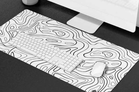 Computer set up with a white keyboard and mouse on a large desk mat with black contour line patterns resembling a topographic map. 