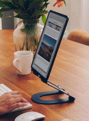 tablet on a metal stand as part of a work set up on a wooden table, with hands typing on a keyboard and a mouse next to it