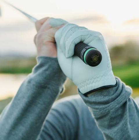 Image of a golfer's hands gripping a golf club with a small device in the end of the club. 