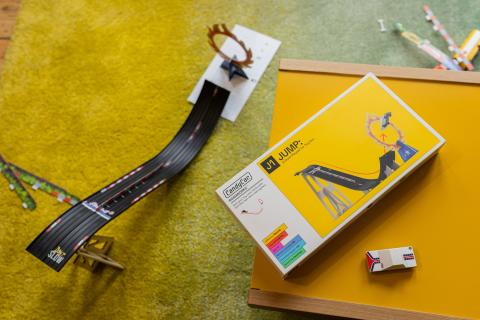 Image of toy track set on a yellow/green carpet. Next to the track is the yellow and white product box featuring an image of the track. 