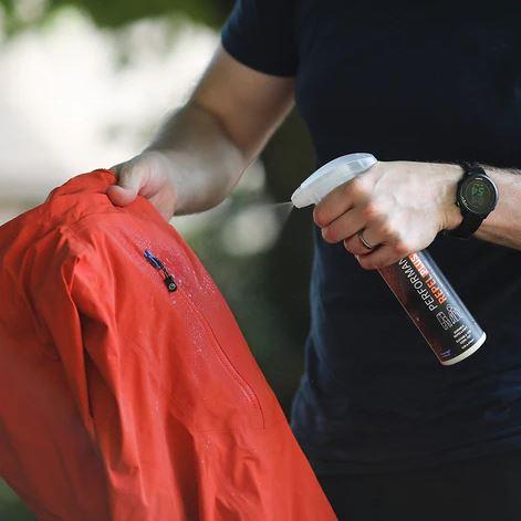 Image Showing a person spraying a red jacket with a waterproofing product labelled 'Performance Repel Plus'. 