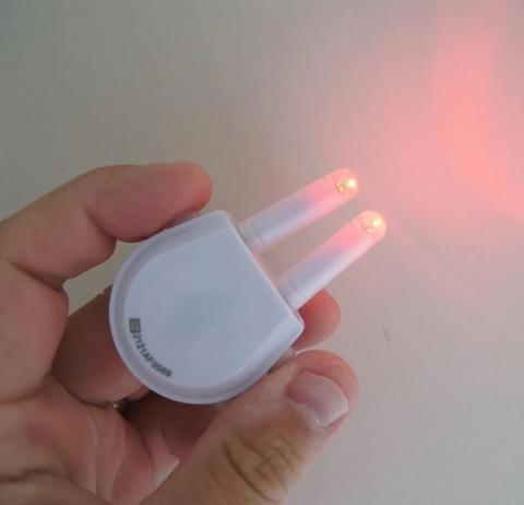 Image of hand holding a small white electronic device, with two prong emitting red light from the tips. 
