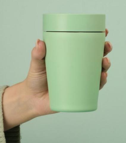 Image of hand holding a light green reusable cup against a light green background. 