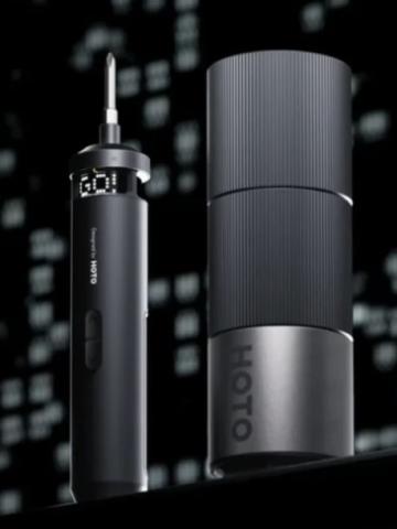 Image of black electric screwdriver with a digital display at the top saying 'Go!', next to a black cylinder screwdriver case. The screwdriver and case are against a black and white blurred pixelated background. 