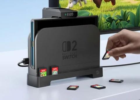 Image of Nintendo Switch in a docking station on a stand with multiple game cards placed around it and a fan at the top. The base features game cards slotted into the platform, with a hand holding a game card next to it.