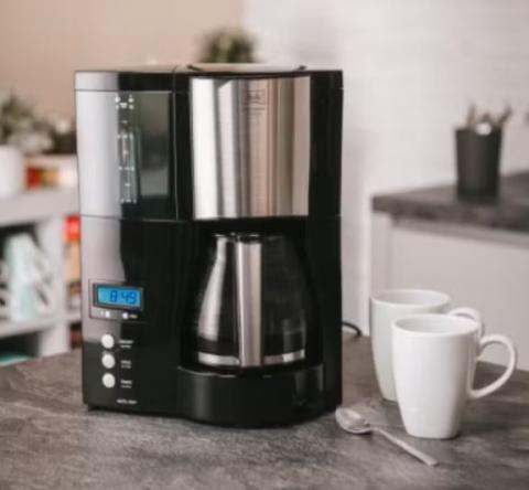 Image of black and stainless steel drip coffee maker on a kitchen counter top, with two white mugs and a spoon beside it. 