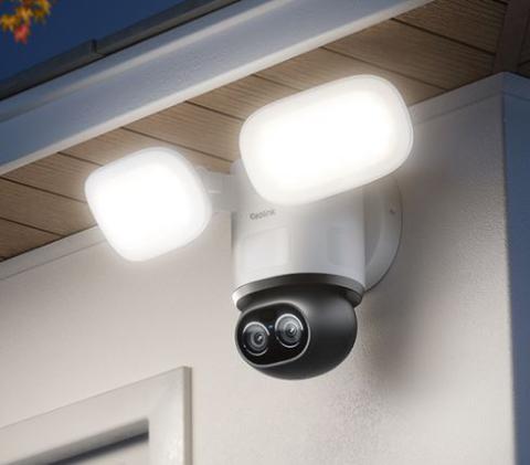 Image of modern outdoor security camera with two bright LED floodlights mounted under a roof eave. 