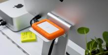 White storage shelf on back of iMac, with orange and white hard drive on shelf