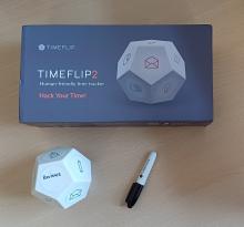 TimeFlip box, with TimeFlip dice covered in activity stickers and marker pen on table 