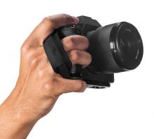 hand holding a small black camera with two fingers looped through a small black camera strap attachment on the side of the camera 