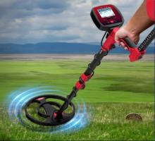 black and red metal detector held up against a field landscape in the background