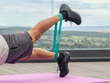 Legs doing an ankle raising exercise with a teal resistance band between them 