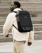 man walking wearing a cream jacket with a black rucksack on his back 