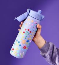 hand holding lilac water bottle with floral pattern on it on a purple background