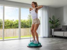 woman standing on a balance trainer pulling resistance bands to her shoulders 