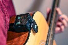 music tutor device clipped on the edge of an acoustic guitar being held by a person 