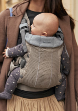 person wearing a grey/beige baby carrier, with a baby in it facing the person