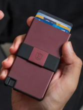 hand holding dark red metal cardholder, with black band around the middle and a few cards poking out the top, all on a black background 