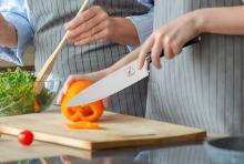 hand holding knife chopping a yellow pepper on a wooden chopping board 