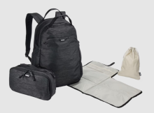 dark grey rucksack, with a smaller bag, grey changing mat and small drawstring bag next to it. All on a whit background. 