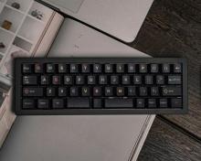 black keyboard with different colour symbols and letters on each key. the keyboard is on a white book on a dark grey wood effect background. 