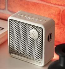 ivory square speaker, with grey front speaker plate with a circular logo on the front 