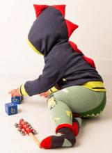 small child playing with blocks facing away from the camera, wearing a navy hoodie with red soft spikes on the back and hood, green leggings and red and black socks