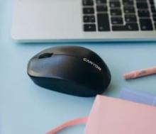 small black computer mouse on a blue table next to a laptop