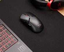 black gaming mouse on a black mouse mat, with a laptop next to it 