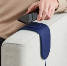 blue silicone pad over arm of white sofa chair, with persons hand placing mobile phone on it