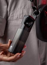 person hand holding a long squared ear bud case with a keyring on one end attaching it to a bag