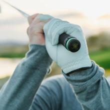 Image of a golfer's hands gripping a golf club with a small device in the end of the club. 